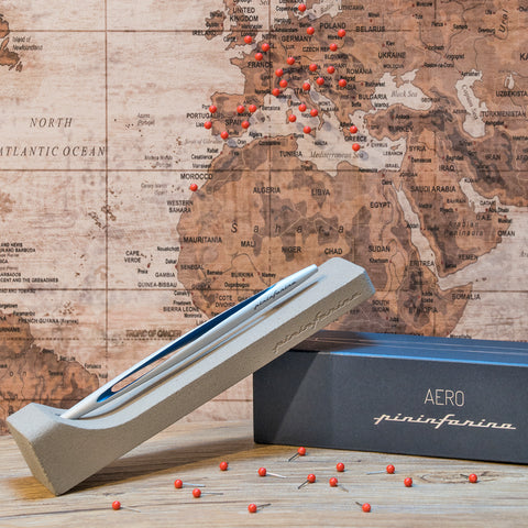 Pininfarina Segno "Aero" inkless pen with ethergraf tip with aluminum silver and blue body in its concrete base with a background of a vintage map.
