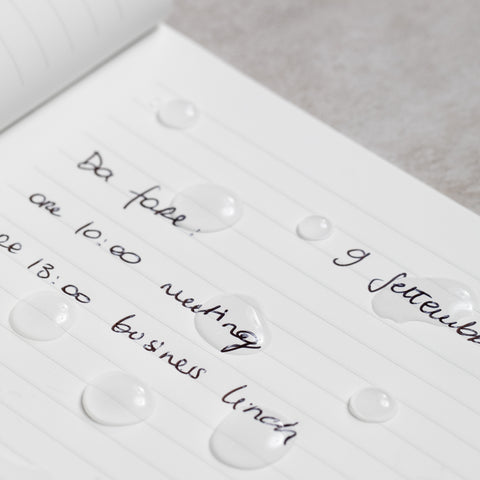 Close up of the Pininfarina Segno "Stone Paper Notebook Oracle Red Bull Racing Edition" in its ruled version with notes written and drops of water, showing that the water doesn't absorb and it's waterproof.