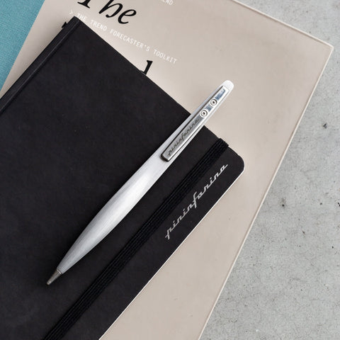 Pininfarina Segno "Space" ethergraf inkless pen with magnesium body in its pure gray version clipped to a Pininfarina stone paper black notebook