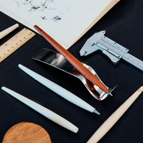 FO - Forever Made In Italy "Piuma Leonardo Special Edition" ethergraf inkless or ballpoint pen in its pear wood steam version, standing in its stainless steel ondulated base, next to other piumas and rulers.