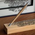 Pininfarina Segno "Cambiano Engine Maserati Special Edition" luxury ethergraf inkless pen with aluminum body and cedar wood inserts standing in its cedar wood base with a drawing of an engine.