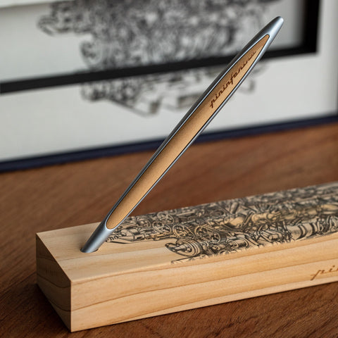Pininfarina Segno "Cambiano Engine Maserati Special Edition" luxury ethergraf inkless pen with aluminum body and cedar wood inserts standing in its cedar wood base with a drawing of an engine.