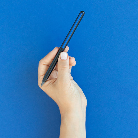 Hand holding a "Grafeex pencil" with black aluminum body and blue clip in a blue background.