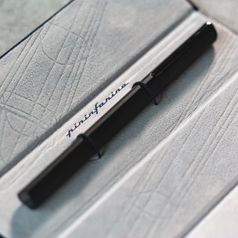 Pininfarina Segno "PF ONE Ballpoint" pen in its black version displayed inside its open packaging. The PF ONE Ballpoint has a triangular grip.