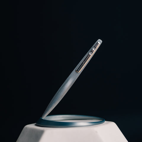 Pininfarina Segno "Space" ethergraf inkless pen with magnesium body in its pure gray version standing in its ellipsoidal aluminum desk base.