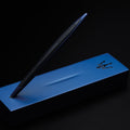 Pininfarina Segno "Cambiano Ink Blu Maserati Edition" ballpoint pen with blue aluminum body and black rubber inserts standing in its blue base with the maserati logo in a black background.