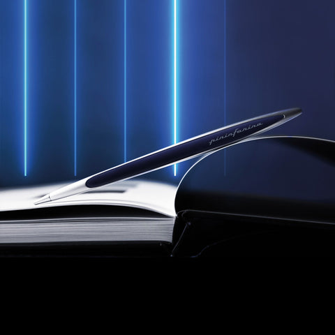 Pininfarina Segno "Cambiano Oracle Red Bull Racing" special edition pen, available in Ethergraf Inkless or ballpoint. Aluminum body with blue painted wood inserts lying in a open 
book with neon blue lights in the background.