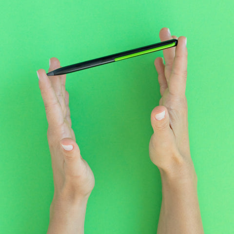 Hand holding a "Grafeex pencil" with black aluminum body and green clip in a green background.