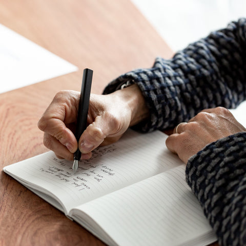 Person writing in a stone paper notebook with the Pininfarina Segno "PF ONE Fountain Pen" in its black version.