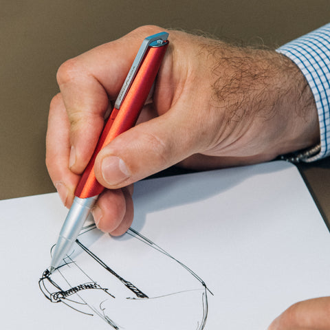 Hand of a man sketching with the Pininfarina Segno "PF GO Rollerball" pen in its red version.