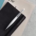 Pininfarina Segno "Space" ethergraf inkless pen with magnesium body in its pure gray version clipped to a Pininfarina stone paper black notebook