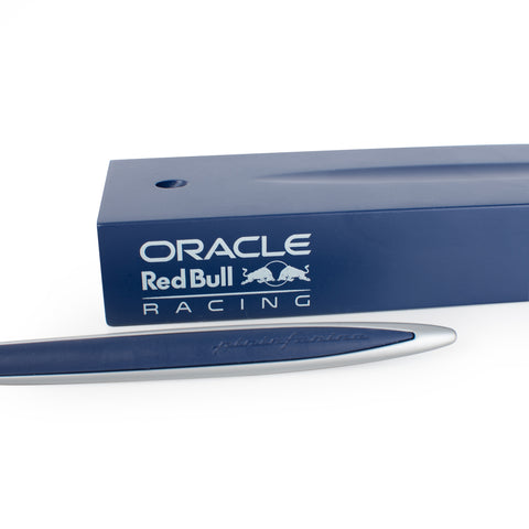 Closeup of the Pininfarina Segno "Cambiano Oracle Red Bull Racing" special edition pen with aluminum body with blue painted wood insert, next to its blue base with the  Oracle Red Bull Racing logo.