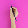 Hand holding a "Grafeex pencil" with black aluminum body and magenta clip in a magenta background.