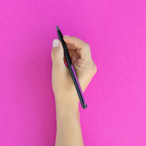 Hand holding a "Grafeex pencil" with black aluminum body and magenta clip in a magenta background.